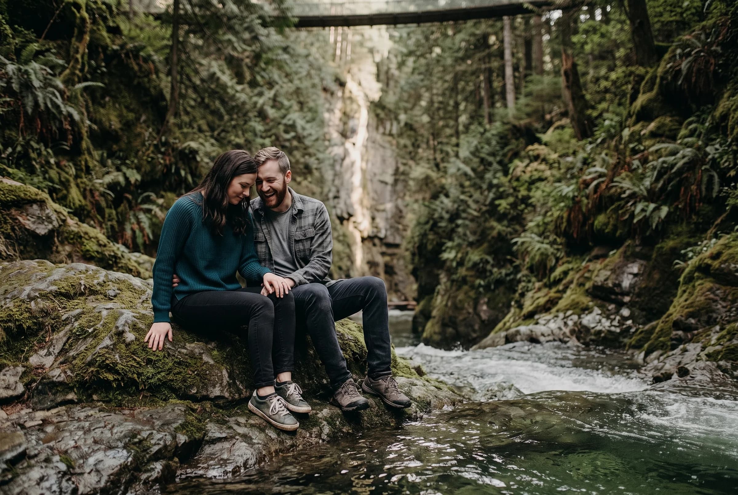 Couple sitting together on a moss-covered boulder on the floor of Lynn Canyon beside green water