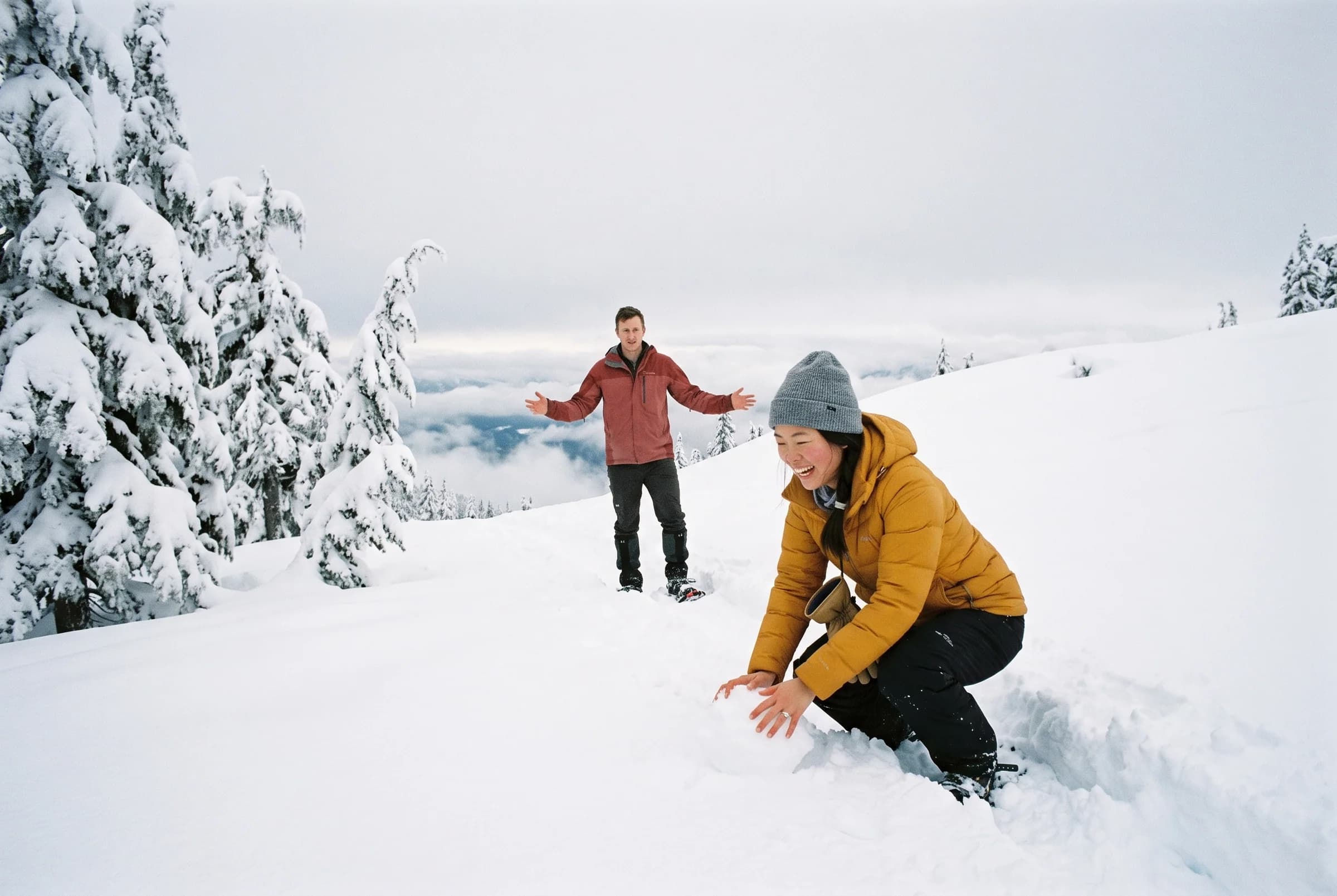 Couple playing in deep snow below snow-laden hemlocks on Mount Seymour