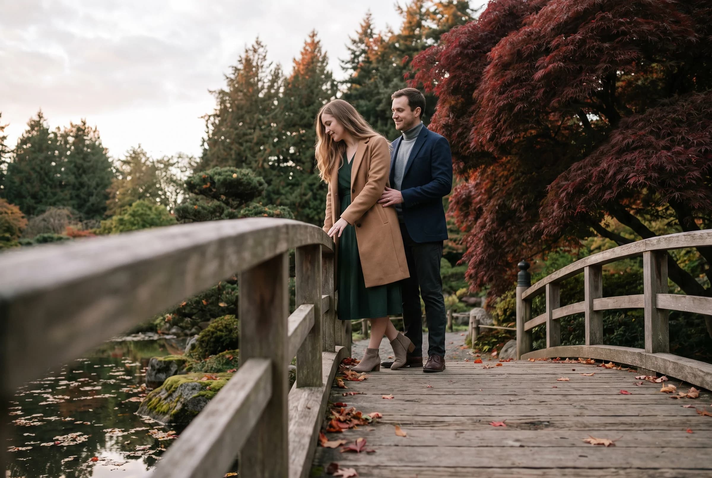 Couple pausing on the arched wooden bridge at Nitobe Memorial Garden with red maples and fallen leaves