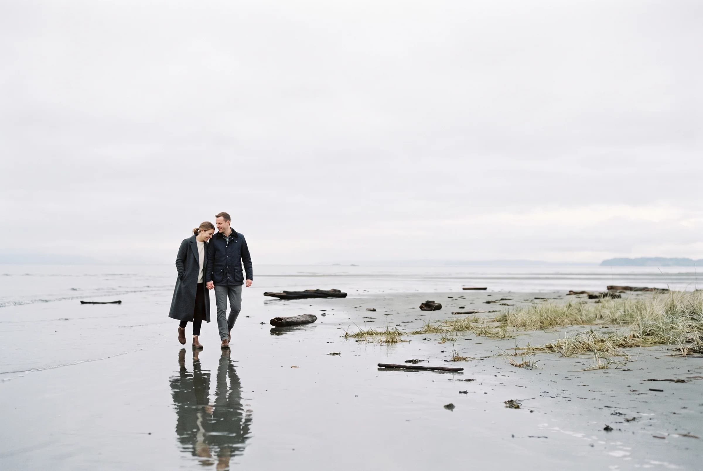 Couple walking on the wet tidal flat at Blackie Spit at blue hour with their reflection in the water