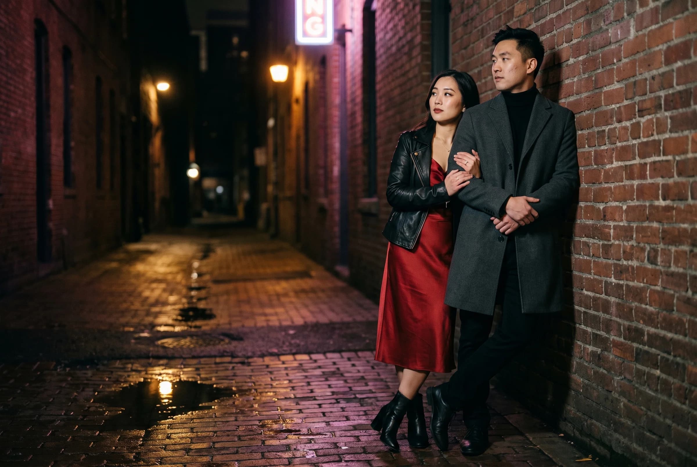 Couple in a brick alley in Gastown at night lit by warm street lamps and neon, with wet cobbles
