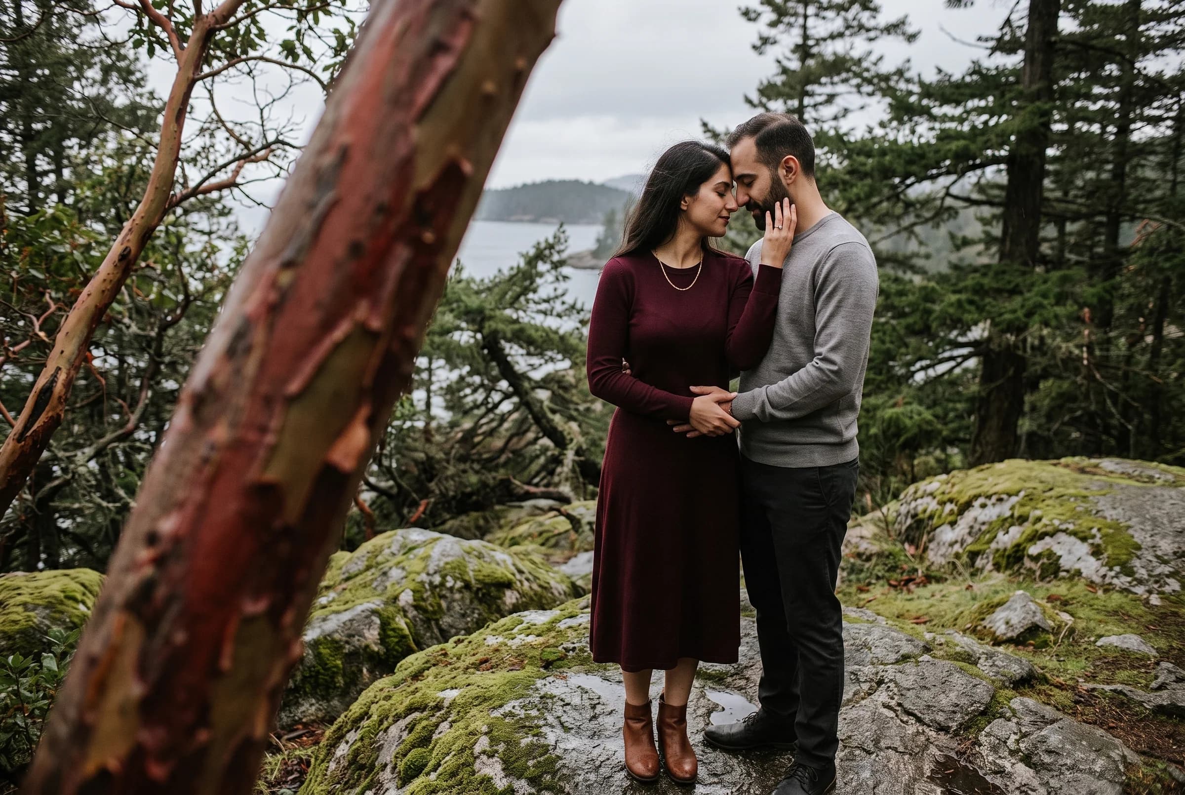 Couple standing close on mossy granite among arbutus trunks at Lighthouse Park after rain