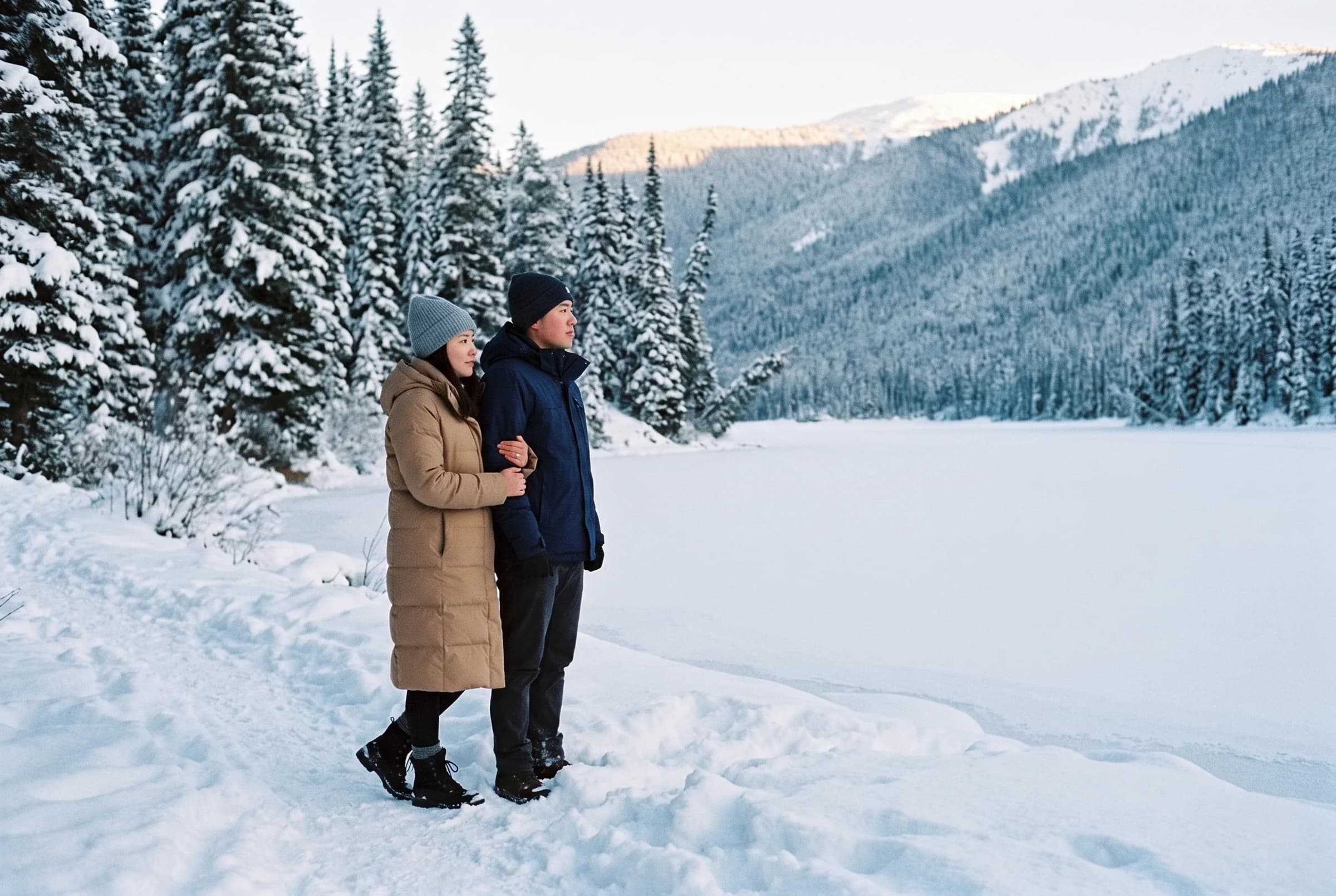 Couple standing on the snowy shore of a frozen Lightning Lake in Manning Park with snow-laden spruce